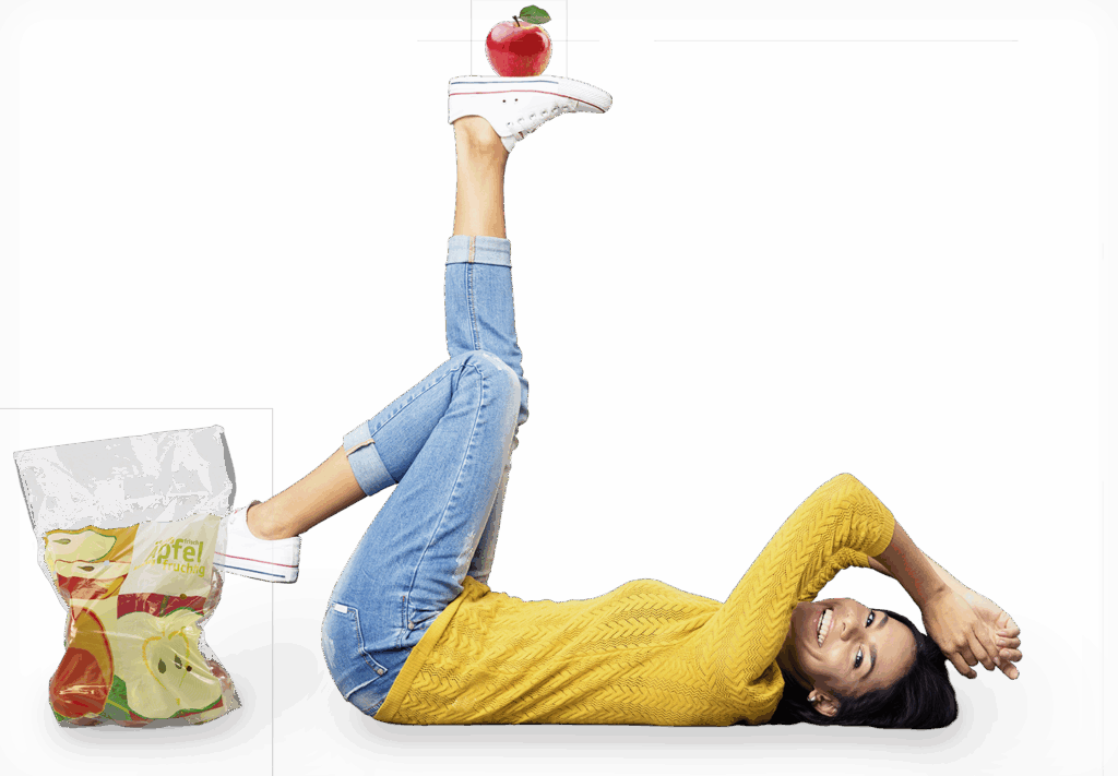 Frau liegt auf Rücken, balanciert einen Apfel und neben ihr steht ein Rollenbeutel für Äpfel